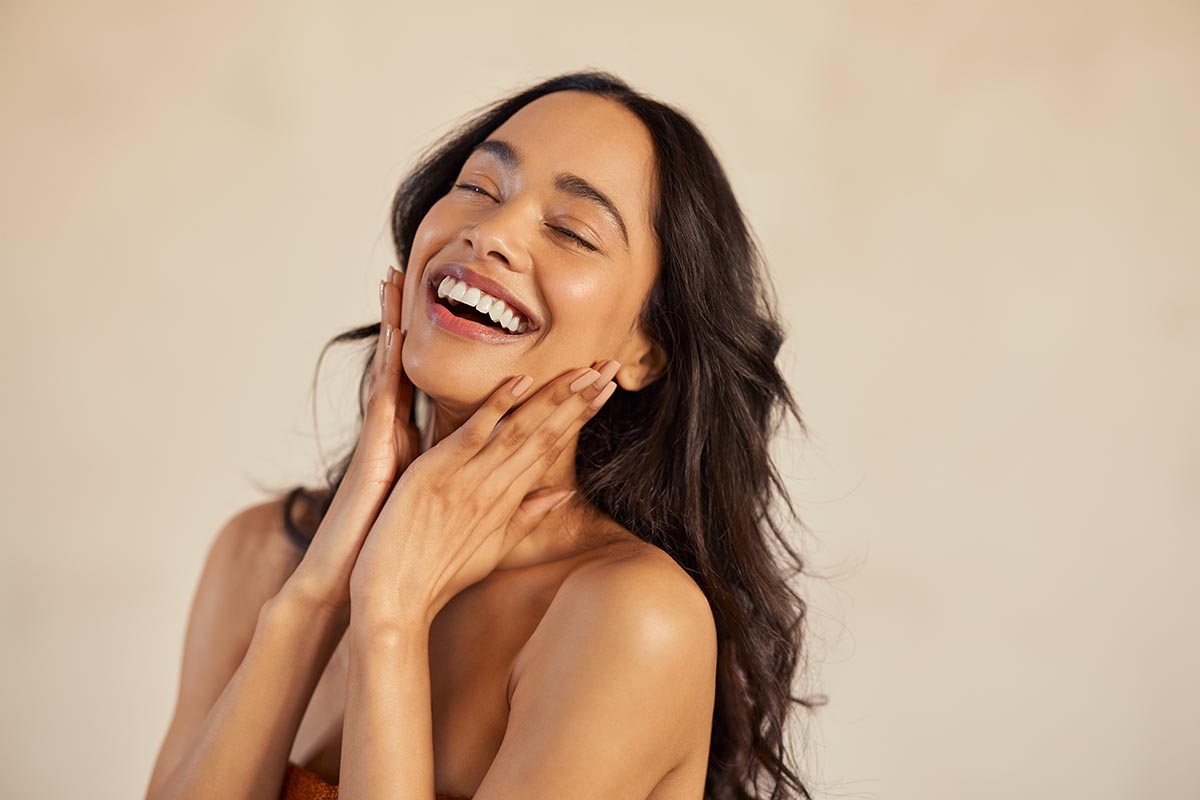 Multiethnic young woman touching her clean and healthy face against background with closed eyes. Latin hispanic woman feeling good with perfet skincare routine. Natural beauty portrait of mexican girl with black long hair.