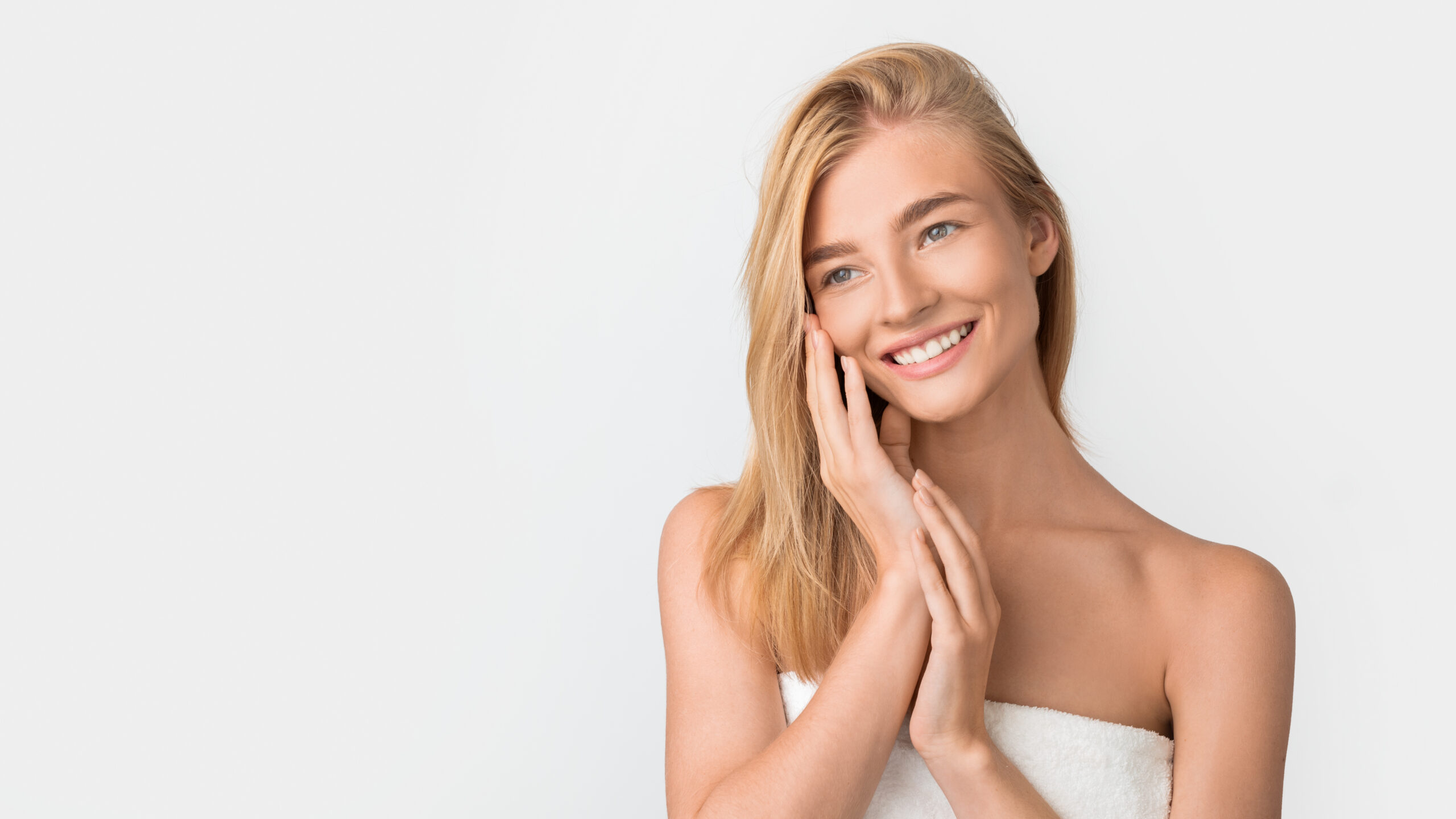 Beautiful blonde woman wrapped in towel touches face, white studio Botox: More Than Just an Aesthetic Treatment